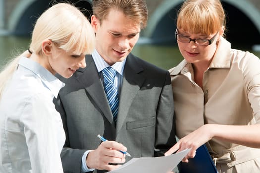 Portrait of friendly business team looking at document in mans hands and talking