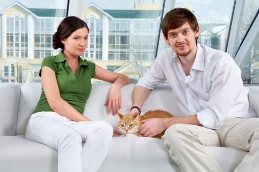 A young couple sitting on sofa with a cat and looking at camera
