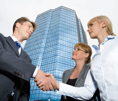 Image of businessman shaking hand to confident woman with another female standing near by
