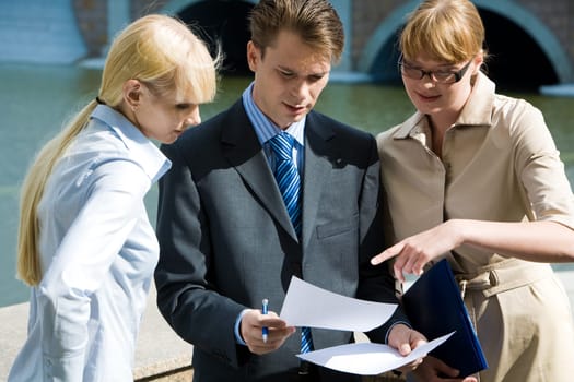Image of confident man holding paper in hands while one of women pointing at it