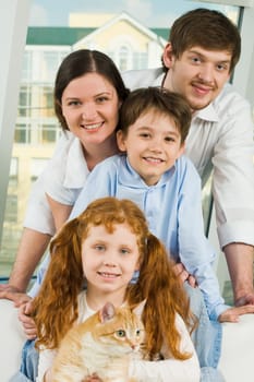 Photo of cheerful siblings with red cat and their parents looking at camera happily