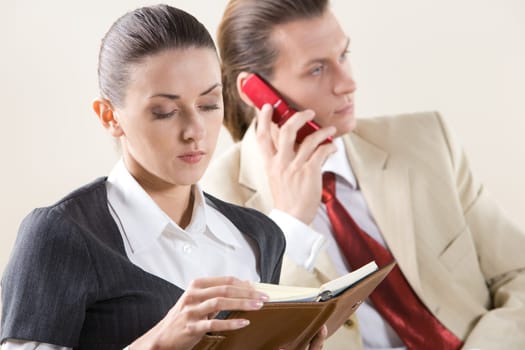 Portrait of pretty employee looking into notebook on background of man talking on the phone