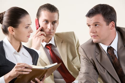 Photo of two colleagues looking at each other during meeting on background of phoning man