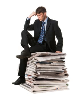 Image of pensive businessman sitting on the stack of newspapers