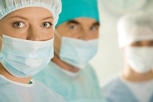 Portrait of female surgeon wearing protective mask on background of her colleagues