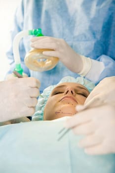 Photo of young female patient with closed eyes before operation with hands of surgeons over her