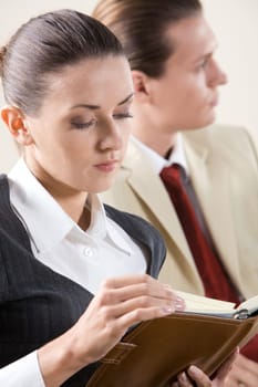 Image of pensive business lady watching into notebook in her hands with man at background