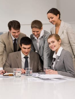 Portrait of successful employees looking at papers while confident woman smiling at camera during meeting