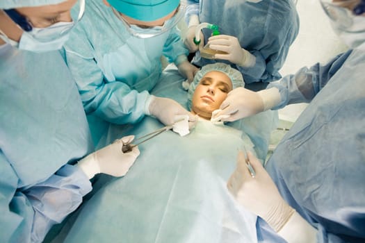 View from above of lying patient with closed eyes and doctors inclining to her
