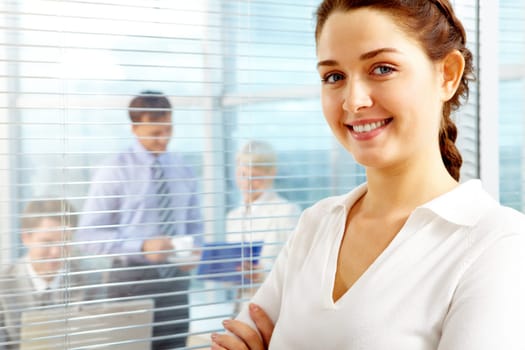 Female leader looking at camera with team of partners working in office behind