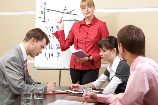 Photo of smart woman pointing at whiteboard at seminar while business partners listening to her