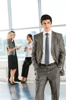 Portrait of smart businessman in suit looking aside on background of interacting co-workers