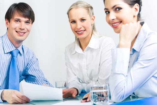 Photo of three friendly specialists sitting at table and looking at camera during work