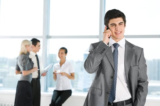Photo of handsome employer calling his partner on background of working people
