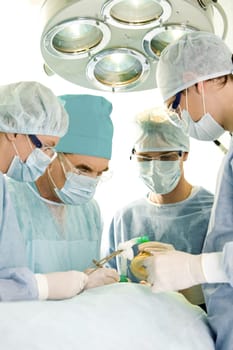 Image of operation: four people in surgical clothes standing near patient