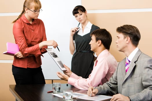 Confident woman pointing at diagram in mans hand while the latter looking at her