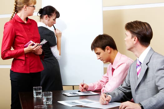 Image of pretty teacher looking at smart student by whiteboard with two men at workplaces