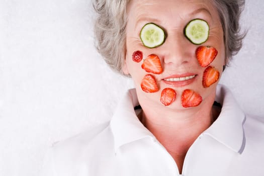 Face of mature woman with cucumber and strawberry slices on it