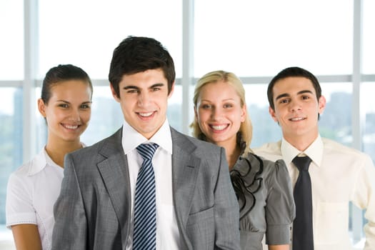 Photo of successful employer looking at camera with his colleagues at background