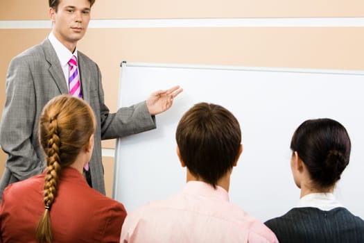Image of serious businessman pointing at whiteboard with three partners listening to him