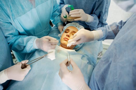 Photo of young female patient lying with closed eyes before operation with hands of doctors over her