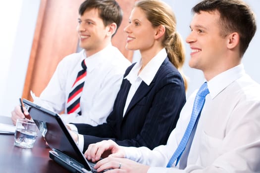 Row of three mature students sitting at the table and looking at a teacher