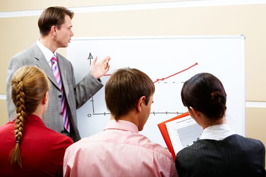 Image of serious businessman pointing at whiteboard with three partners listening to him