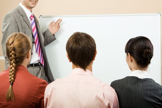 Rear view of business partners listening to lecturer and looking at whiteboard