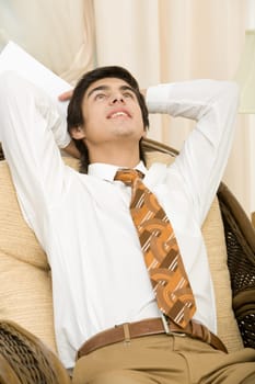 Portrait of positive man relaxing in arm-chair with hands behind head
