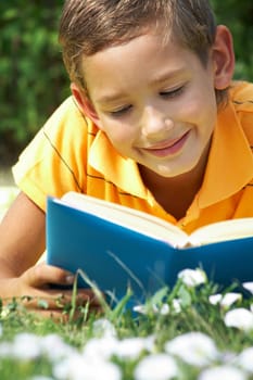Portrait of cute schoolboy reading interesting book in natural environment