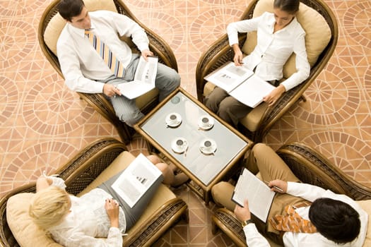 View from above of business people in armchairs reading documents