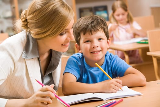 Photo of happy schoolboy looking at camera with teacher near by