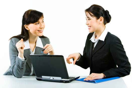 Portrait of two smiling business ladies sitting at laptop pointing at its screen and looking at each other