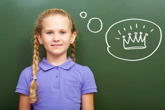 Portrait of smart girl by the blackboard thinking of crown and looking at camera