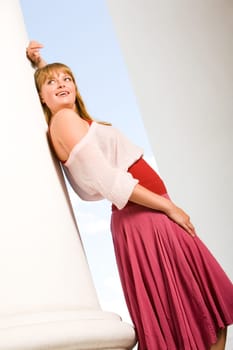 Photo of fashionable woman standing near column on background of blue sky at summer