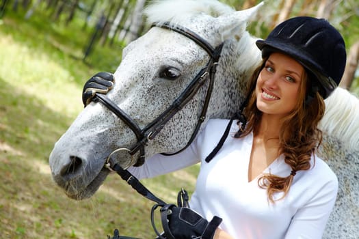 Image of happy female in riding cap embracing purebred horse and looking at camera