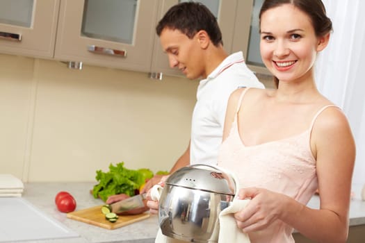 Portrait of happy female with pan looking at camera while her husband cooking salad on background