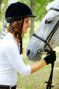 Image of happy female in riding cap holding purebred horse by bridle and looking at it