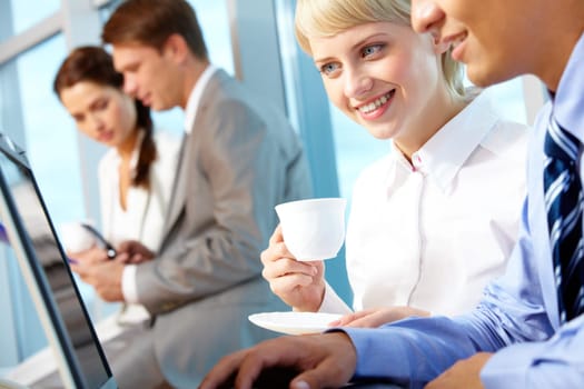 Portrait of young female with cup of coffee looking at laptop monitor in office and interacting with partner