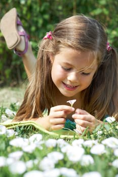 Close-up of girl lying on green grass and enjoying nice smell of tiny flower