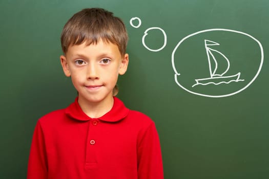 Portrait of smart lad by the blackboard thinking of sail and looking at camera