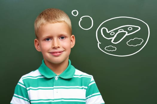 Portrait of smart lad by the blackboard thinking of airplane and looking at camera