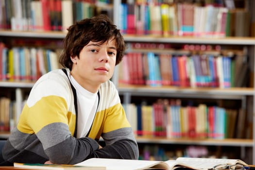 Portrait of clever student sitting in front of open book in college library
