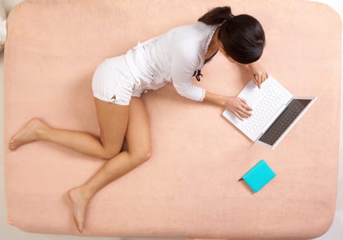 View from above of girl lying on bed and typing on laptop