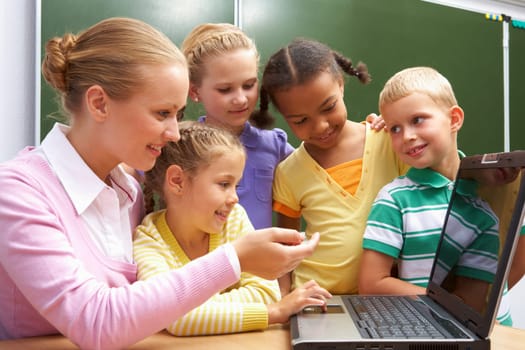 Portrait of pupils looking at the laptop while listening to teacher explaining something