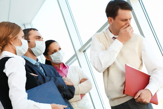 Group of associates in protective masks looking strictly at coughing man