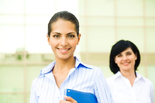 Portrait of pretty employee smiling at camera with her colleague at background