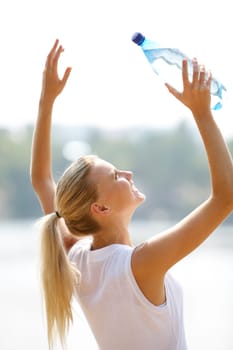 Portrait of pretty blonde with bottle of water raising arms on summer day