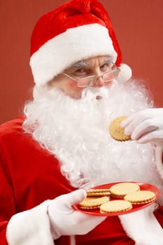 Photo of happy Santa Claus in eyeglasses looking at camera while eating biscuit