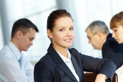 A young businesswoman smiling against working colleagues